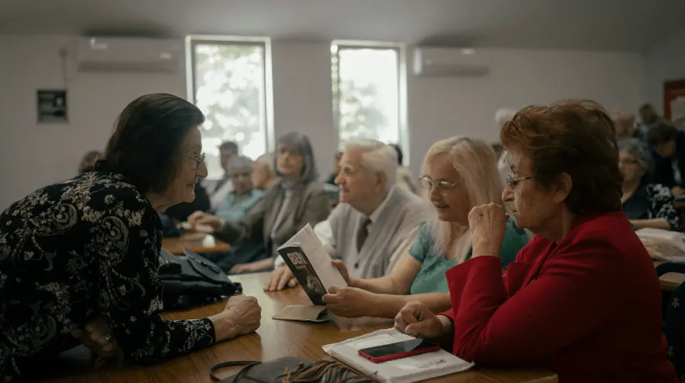 Older persons sit behind tables at a literary workshop.