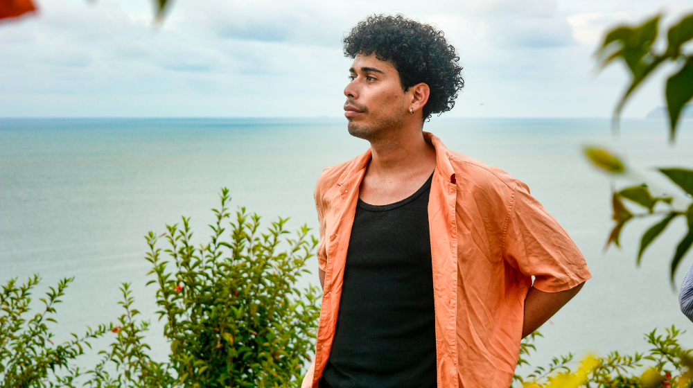 Un joven en una camisa naranja frente al mar