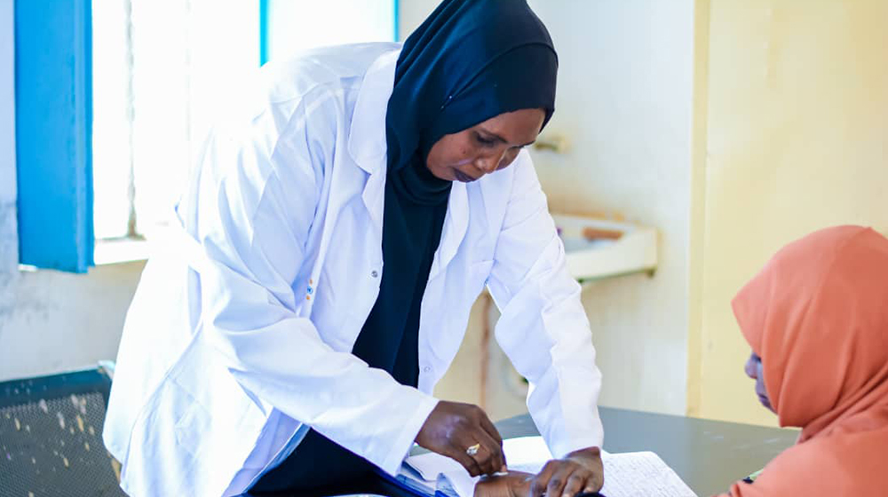 A female healthcare worker places her hand and a medical device on a female patient.