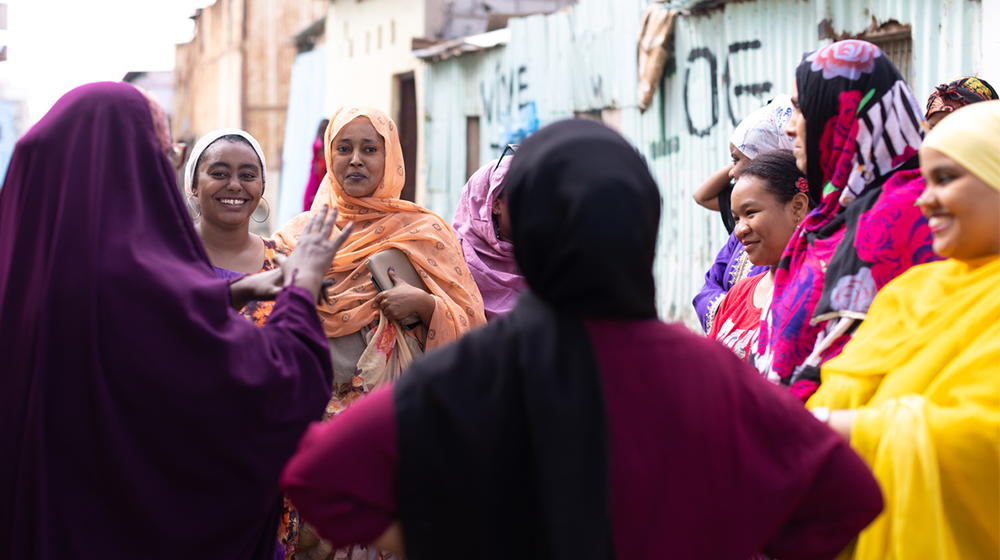 Un groupe de femmes sourit et discute dehors.