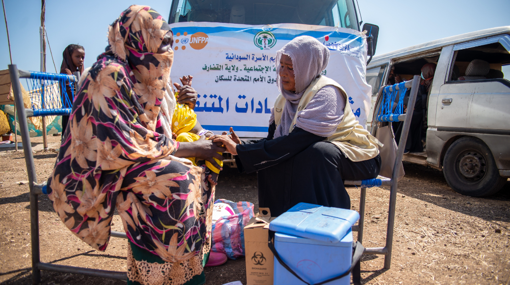 A woman sits outside consulting with a female member of a UNFPA mobile health team.