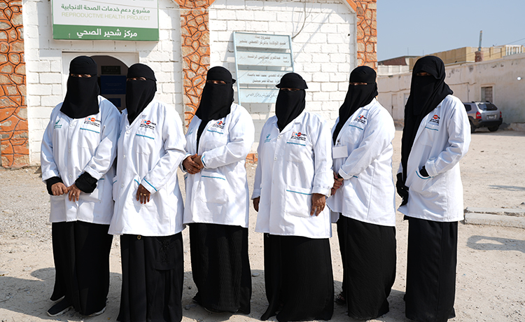 Six femmes, toutes sages-femmes, se tiennent debout devant un bâtiment.