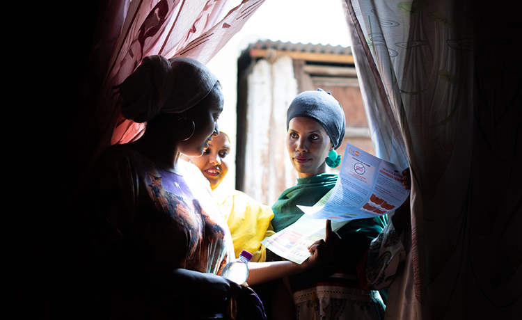 Two women stand in the doorway of another woman’s home, handing her an information leaflet.