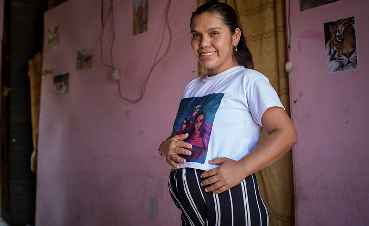 A pregnant mother stands with her hand caressing her womb.