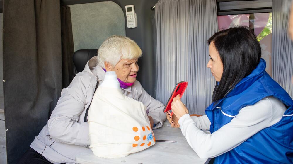 An older woman looks at the mobile phone of a UNFPA worker. 