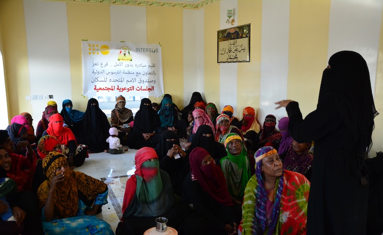 A woman speaks to a group of women seated inside.