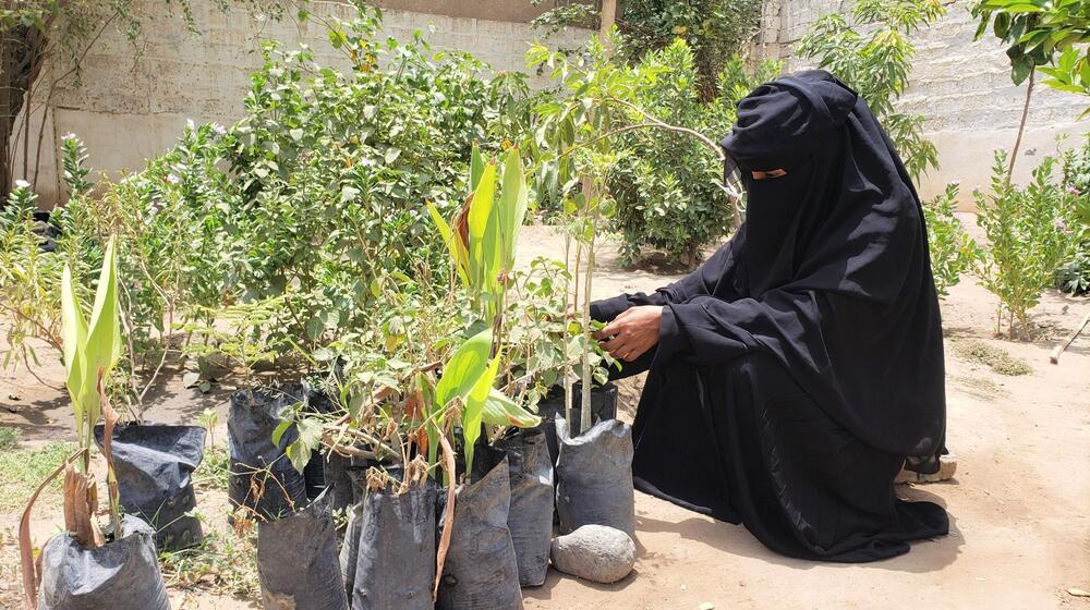 Une femme agenouillée dans une ferme, en plein air, en train de s’occuper de plants de fruits et de légumes.