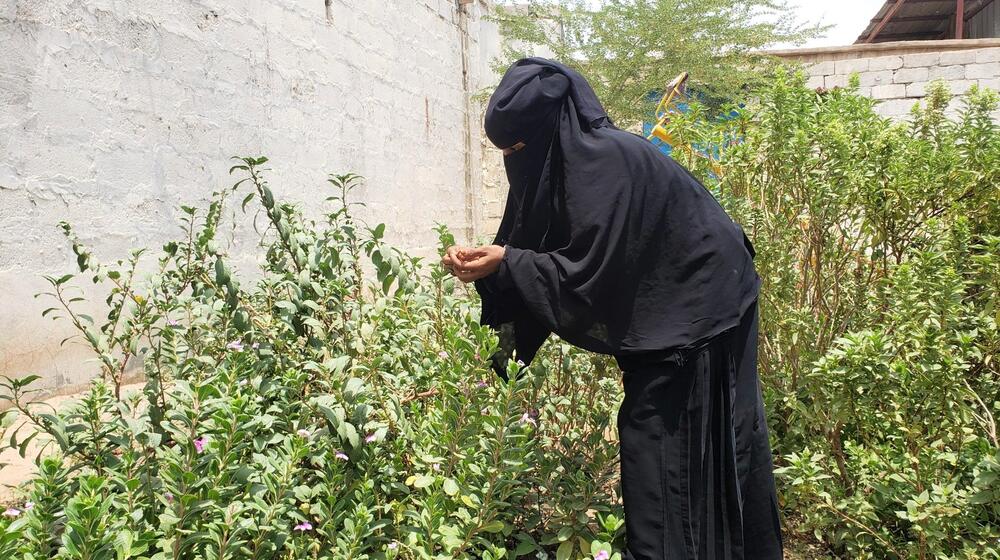 Une femme penchée sur des plantations hautes, dans une ferme de plein air.