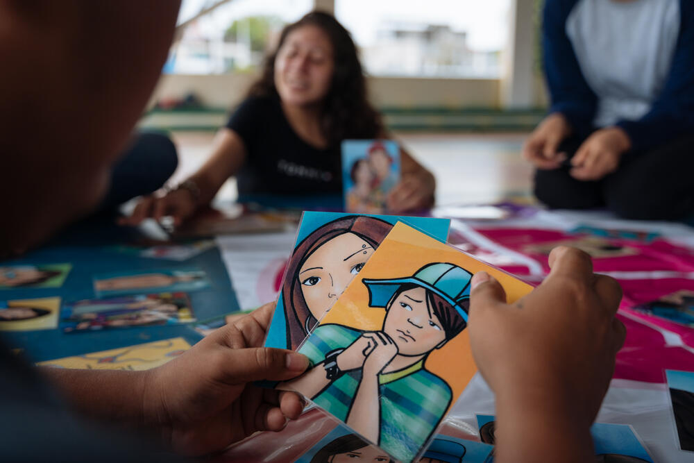 Un groupe de personnes s’assoient à une table et jouent à un jeu de cartes. Les cartes montrent des dessins de personnes montrant différentes émotions.