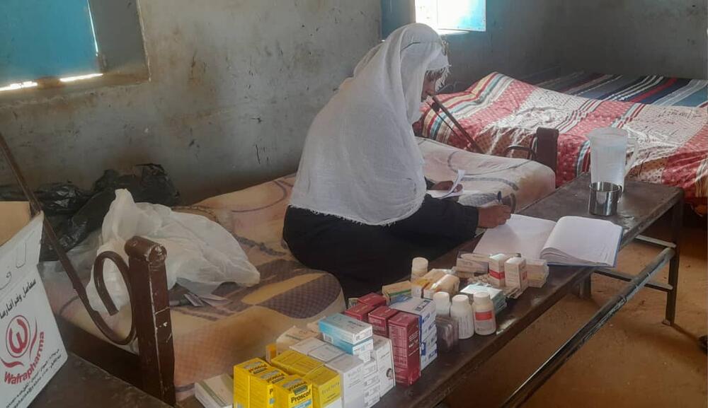 A woman sits on a bed taking notes beside a table of medications