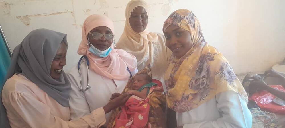 A midwife holds a newborn, surrounded by three smiling women.