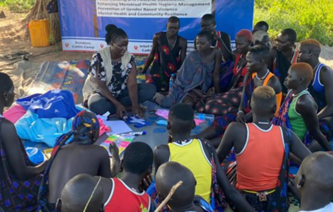 Des femmes et des filles assises par terre en cercle, écoutant une autre personne parler.