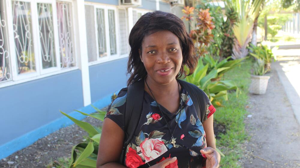 A female teacher stands in front of a school building.