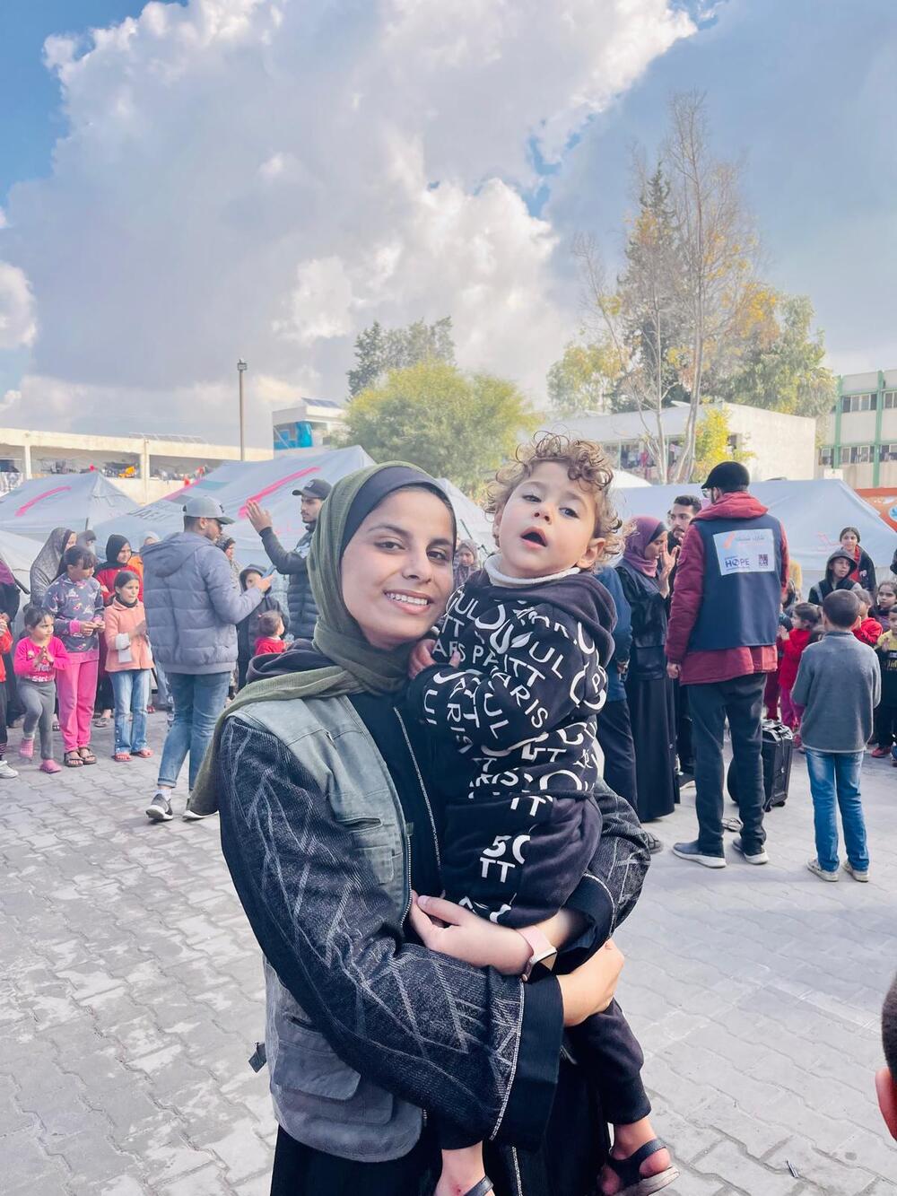 A young woman holds a child in front of tents