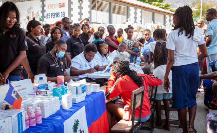 Une foule est réunie autour d’agent·e·s de santé assis·e·s à une table et remplissant des ordonnances]