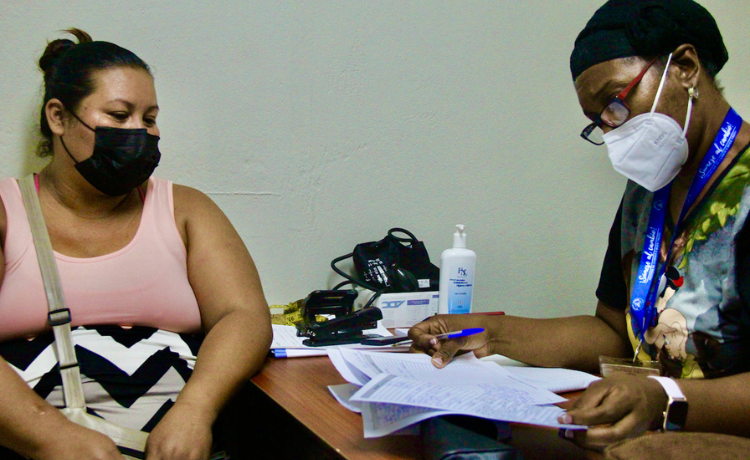  A woman sits at a desk in front of another woman consulting papers