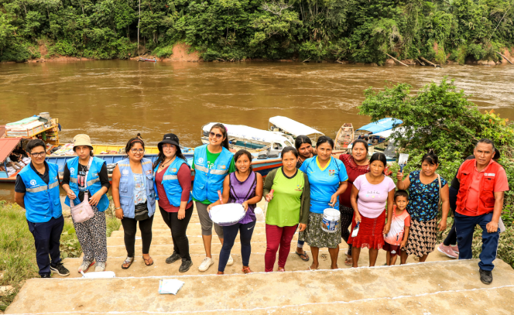  Un groupe de 14 personnes regardent l’objectif. Certaines portent des vestes bleues de l’UNFPA, d’autres tiennent des seaux de peinture blanche. Elles se tiennent toutes sur les marches du port au milieu de la jungle.