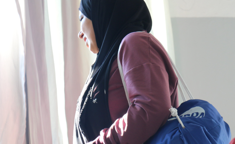  Une femme vêtue d’un foulard noir et d’un gilet rose porte un sac bleu à cordon de serrage, floqué d’un logo de l’UNFPA.