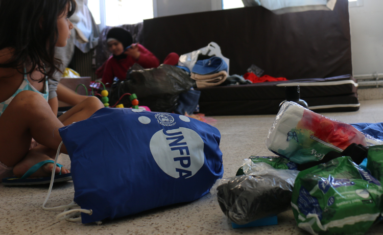 Una bolsa azul con logotipo blanco del UNFPA puesta de lado junto a una pequeña pila de toallas sanitarias y otros artículos de higiene.