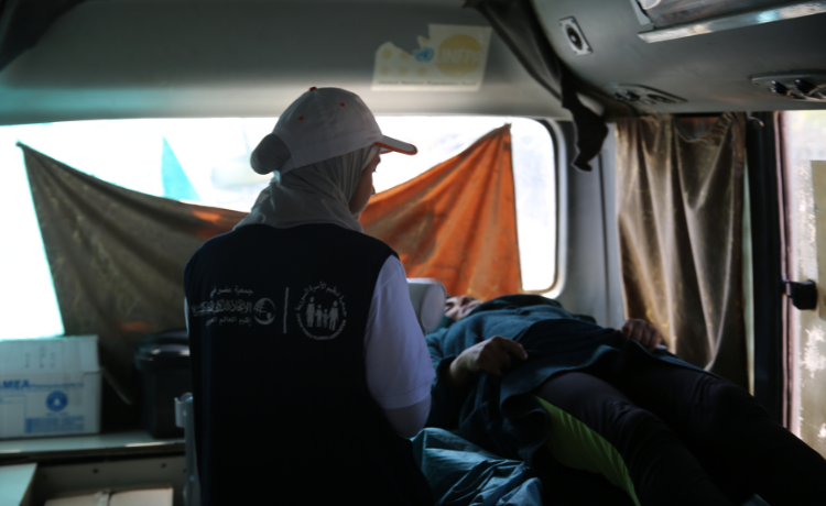  Dans une clinique mobile, une agente de santé portant un gilet bleu et une casquette blanche est assise, veillant sur une femme allongée.