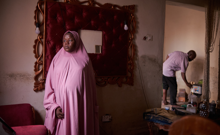 A woman in a pink hijab looks at her home, which is damaged from flooding.