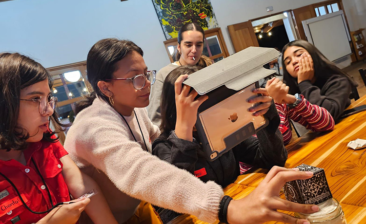 A group of young people sit at a table. One of them is holding a tablet computer.