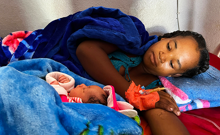 A female patient lies on a bed with her newborn