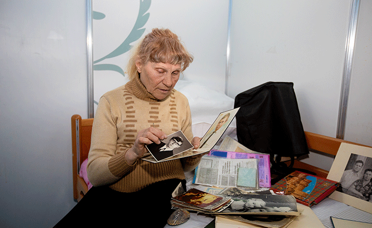 Une femme agée s'assied sur le lit regardant des photographies