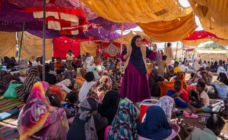 A woman in a UNFPA vest addresses a crowd of seated women under a tent