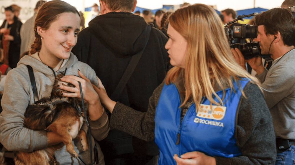 A woman holding her dog is comforted by another woman. 