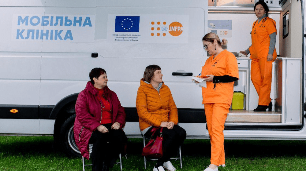 Staff at a mobile health clinic attend to two women. 