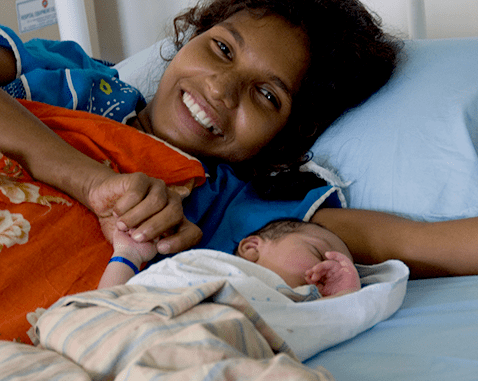 A mother lies next to her newborn baby.