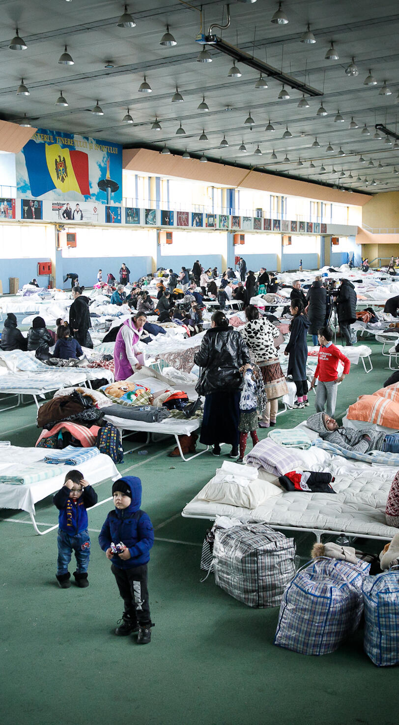 Women and children inside a gymnasium with makeshift beds. 