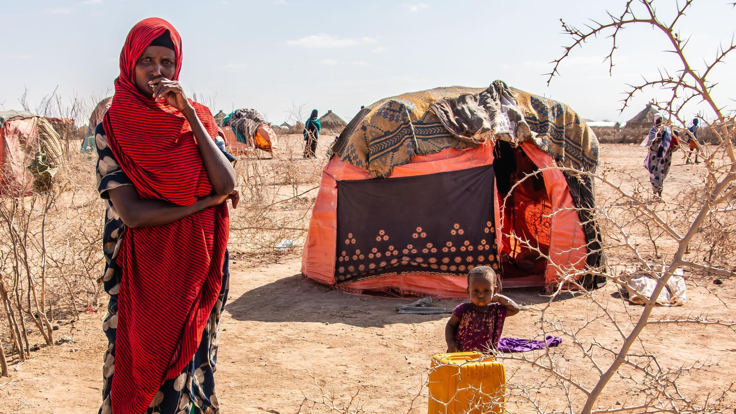 A woman and a small child stand in front of a tent.