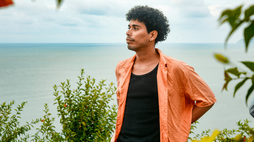 Un jeune homme debout portant une chemise orange regarde la mer