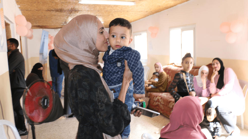 A woman in a pink headscarf nuzzles her toddler son in a clinic waiting room.