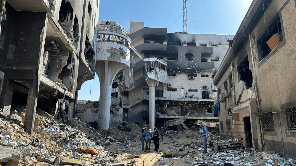 Cuatro personas con chalecos de la ONU de pie entre los escombros de un edificio destruido