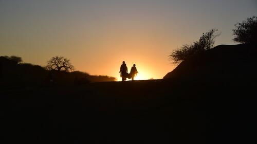 Deux femmes portent un panier et marchent dans un paysage de collines au crépuscule