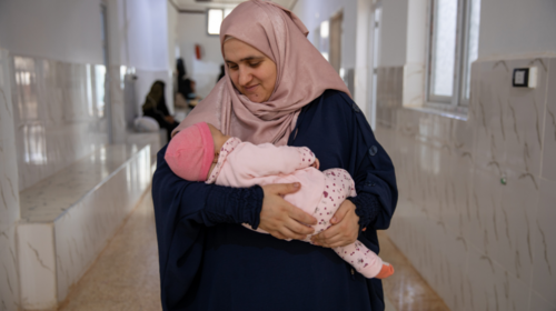  A smiling woman holds a young baby in the corridor of a hospital